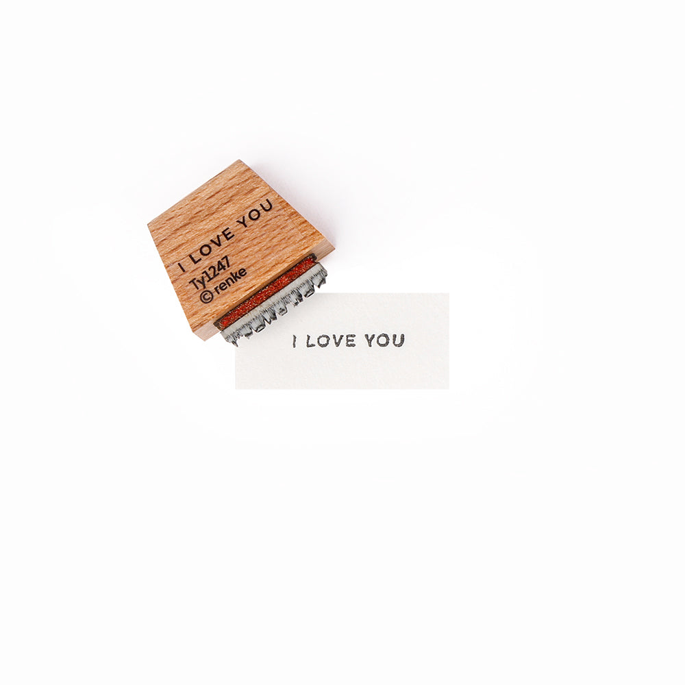 Ein Alexandra Renke Holzstempel und eine Karte zeigen beide das Mini Typo I Love You Design mit "I LOVE YOU" auf weißem Hintergrund.