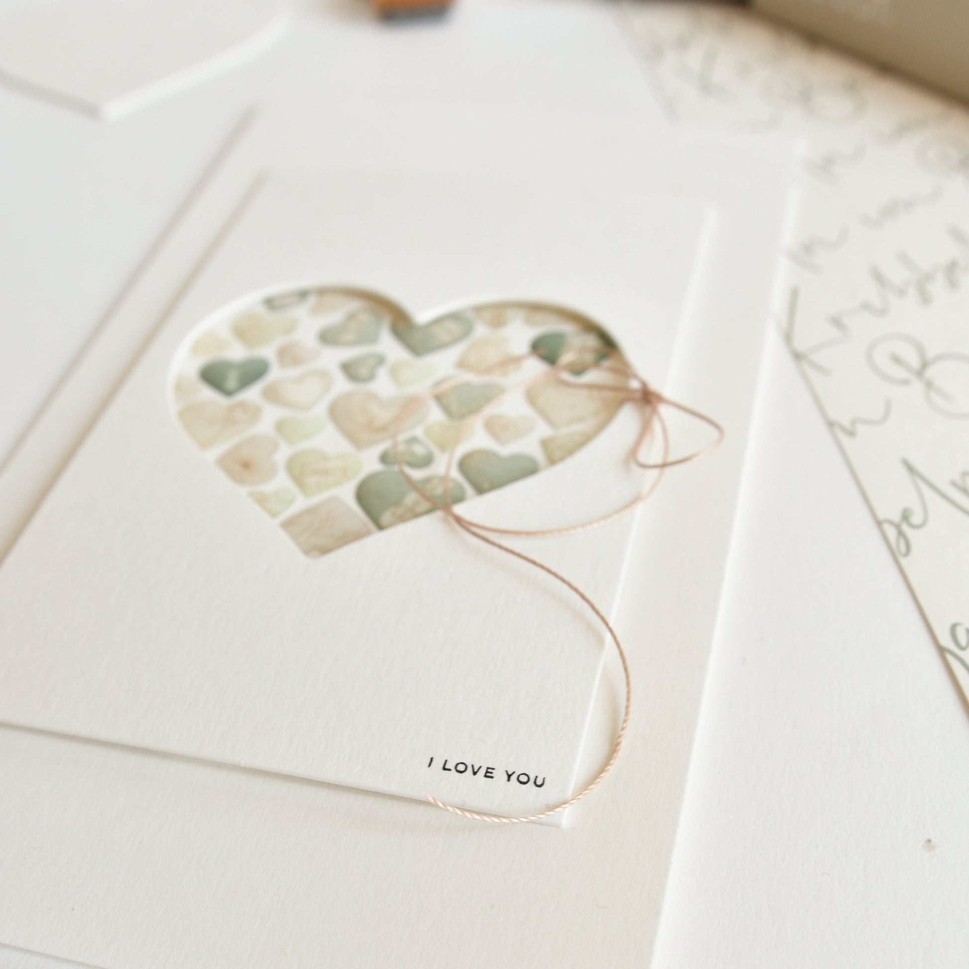 Eine Herzkarte mit pastellfarbenen Herzen im Inneren, einer Kordel und dem Schriftzug "I LOVE YOU" am unteren Rand - perfekt als Mini Alexandra Renke I Love You Geschenk zum Andenken.
