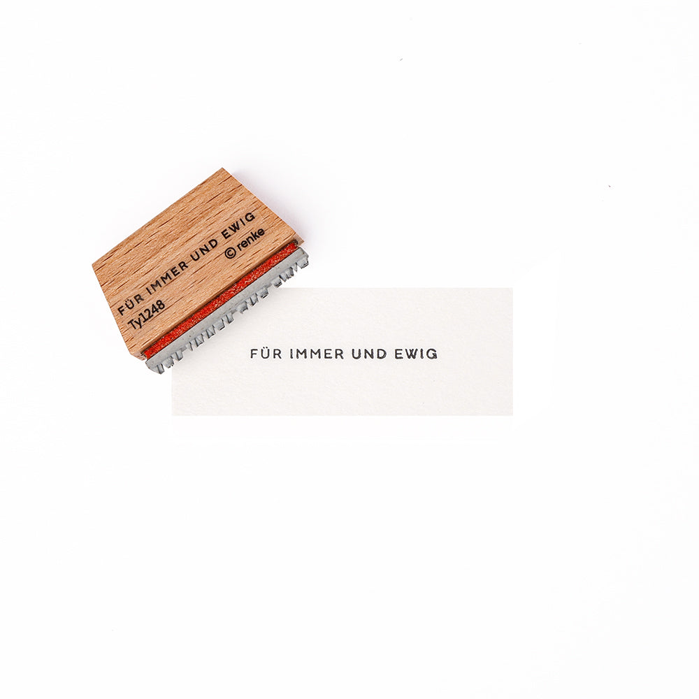 Alexandra Renke Holzstempel und Papier mit dem deutschen Text "FÜR IMMER UND EWIG" unter Verwendung der Mini Typo Für Immer und Ewig Stempelgummi, dargestellt auf weißem Hintergrund.