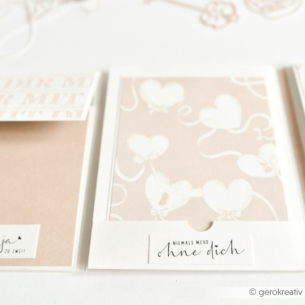 Eine Grußkarte von Alexandra Renke mit weißen herzförmigen Luftballons auf zartrosa Hintergrund und einem deutschen Textetikett, ideal für Papierprojekte.