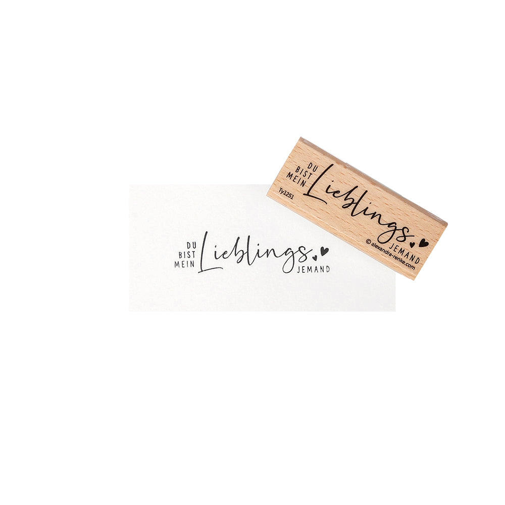 Ein Holzstempel von Alexandra Renke aus hochwertigem Holz mit dem Motiv "Du bist mein Lieblingsmensch" und kleinen Herzillustrationen.