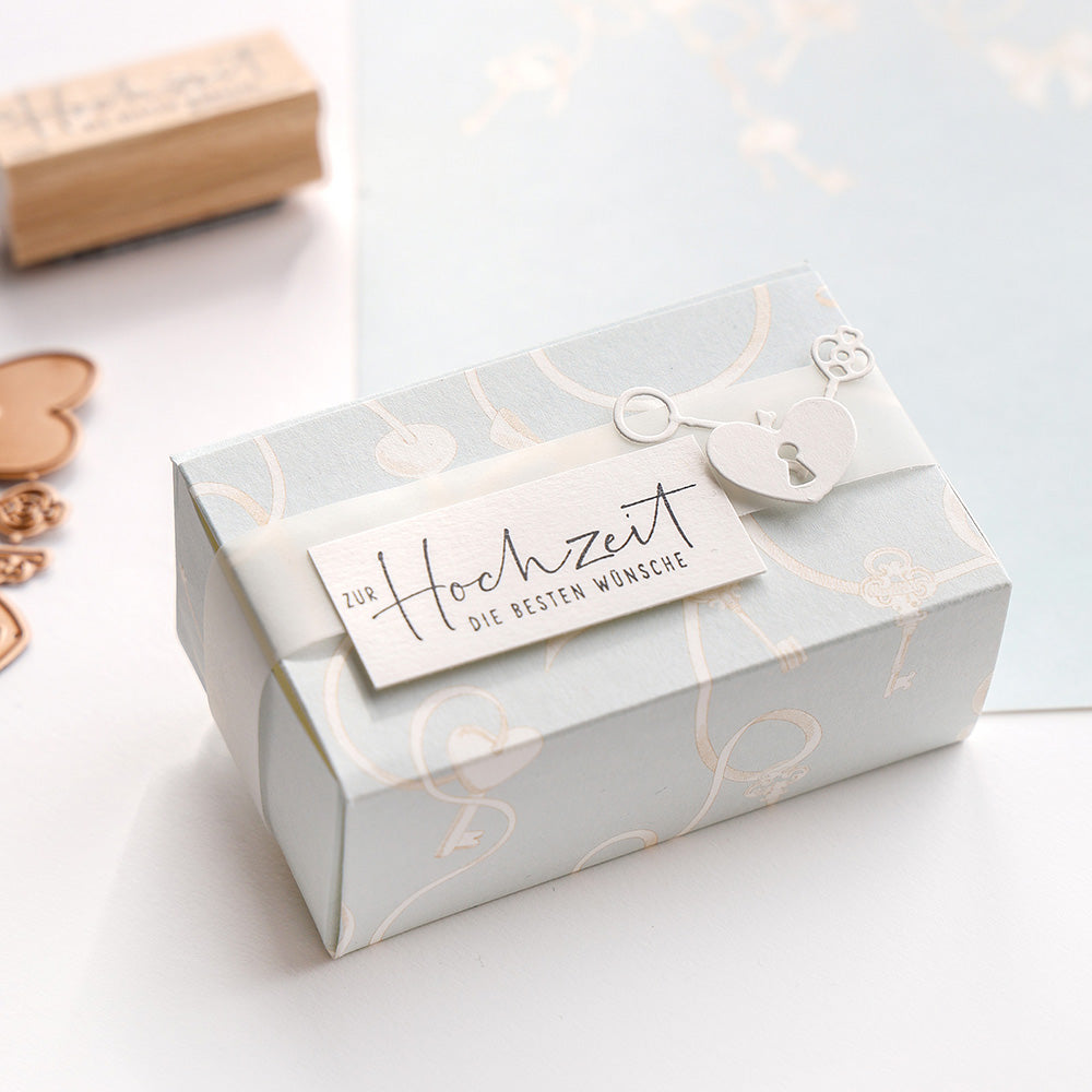 Alexandra Renke-Geschenkbox mit herzförmigem Verschluss, einem Anhänger mit der Aufschrift "zur Hochzeit die besten Wünsche" und einem "Stempel zur Hochzeit" für eine elegante Hochzeitsnote.