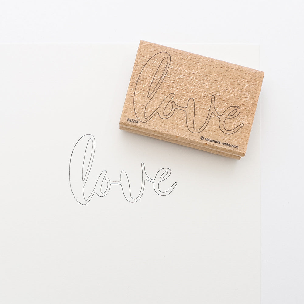 Ein Holzstempel zum Besticken von Alexandra Renke mit dem Wort "Liebe" und dessen Umriss mit Stempelfarbe für Stoff auf weißem Papier - ideal für kreative Stickprojekte und zum Personalisieren Ihrer Bastelarbeiten.