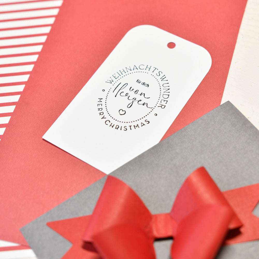 Alexandra Renke's White Christmas Geschenkanhänger mit deutschem und englischem Text, dargestellt auf rotem und grauem Geschenkpapier mit einer roten Schleife - ideal für Ihr Weihnachtswunder oder festliche Papierprojekte.
