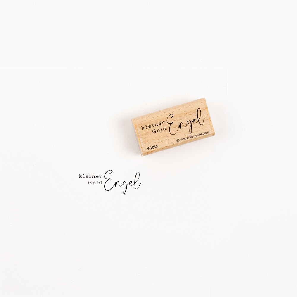 Ein Holzstempel mit der Aufschrift kleiner Gold Engel und seinem Stempelabdruck.