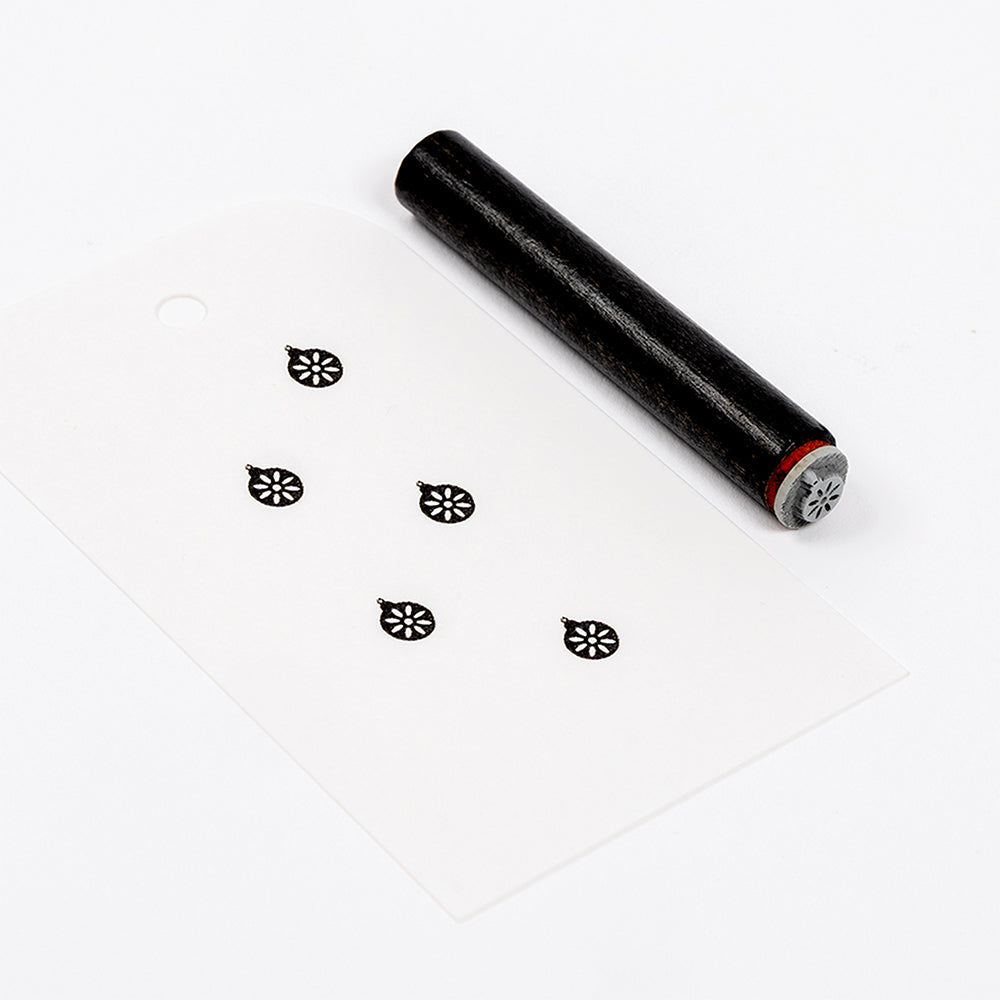 Ein schwarzer Akzentstempel und eine weiße Karte mit fünf blumenförmigen Stempelabdrücken.