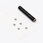 Ein schwarzer Holzstempel und ein weißes Etikett mit fünf aufgestempelten Starburst-Motiven.
