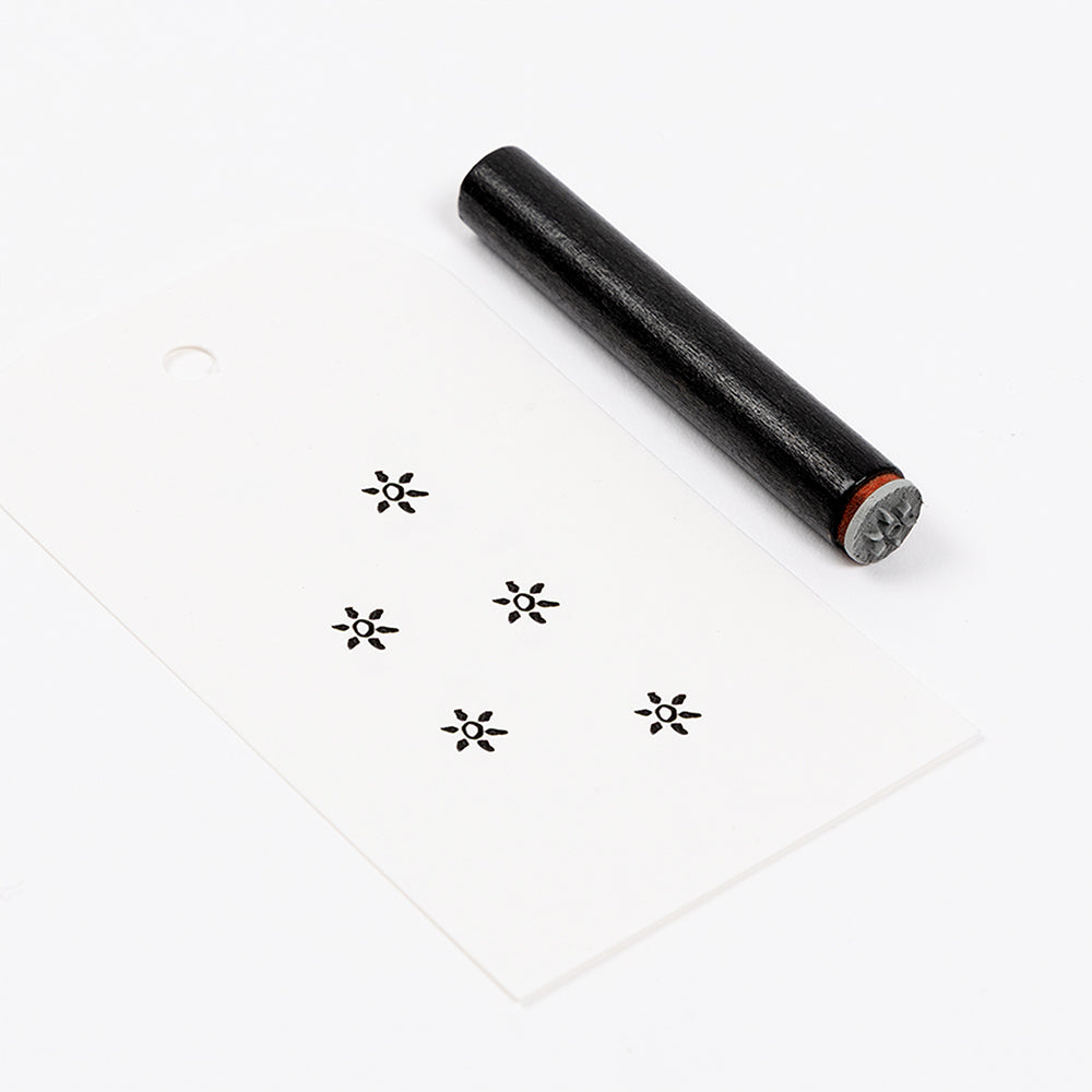 Ein schwarzer Holzstempel und ein weißes Etikett mit fünf aufgestempelten Starburst-Motiven.