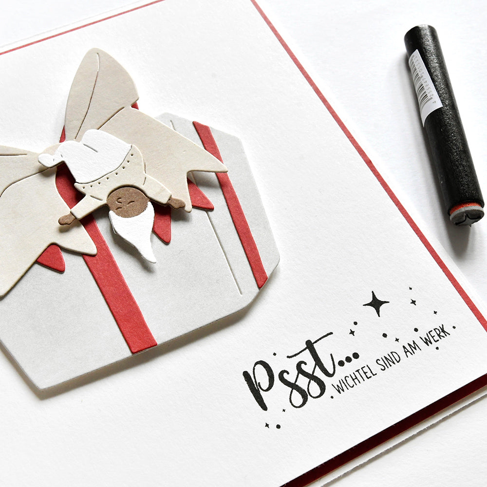 Eine handgefertigte Karte von Alexandra Renke mit einem Wichtel auf einer Geschenkbox und dem Spruch "Pst... Wichtel sind am Werk!", gestaltet mit Motivstempeln.