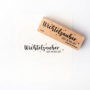 Ein Holzstempel von Alexandra Renke mit Stempelgummi zeigt den Text "Wichtelzauber liegt in der Luft" und kleine Sterne - ideal für zauberhafte Papierprojekte.