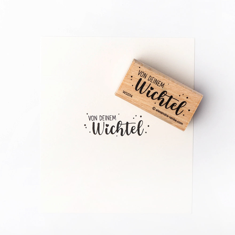 Ein Holzstempel und Papier von Alexandra Renke mit dem deutschen Text "Von deinem Wichtel" in schwarzer Schrift - liebevoll aus hochwertigem Holz gestaltet mit charmantem Stempelmotiv.