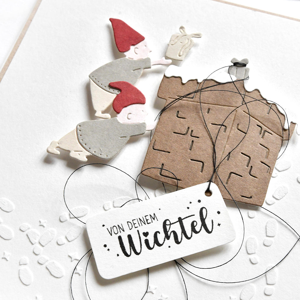 Zwei ausgeschnittene Zwerge drücken eine Geschenkbox; auf dem Anhänger steht "Von Deinem Wichtel". Schwarzer Faden akzentuiert die Karte von Alexandra Renke, ideal für Papierprojekte oder in Kombination mit Ihrem Lieblingsholzstempel.