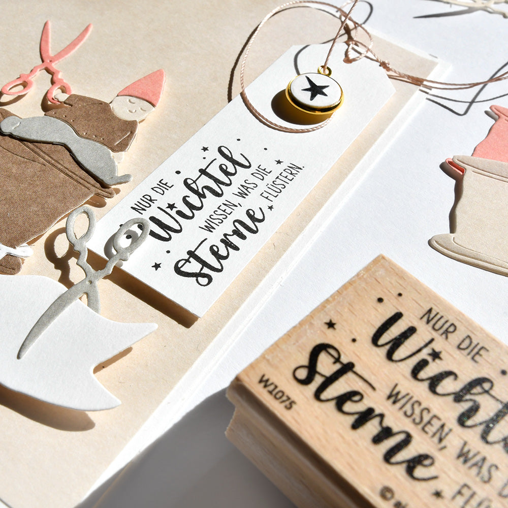 Nahaufnahme von Weihnachtsbasteleien, Anhängern und hochwertigen Stempeln mit deutschem Text von Alexandra Renke, neben Scheren und festlicher Dekoration.