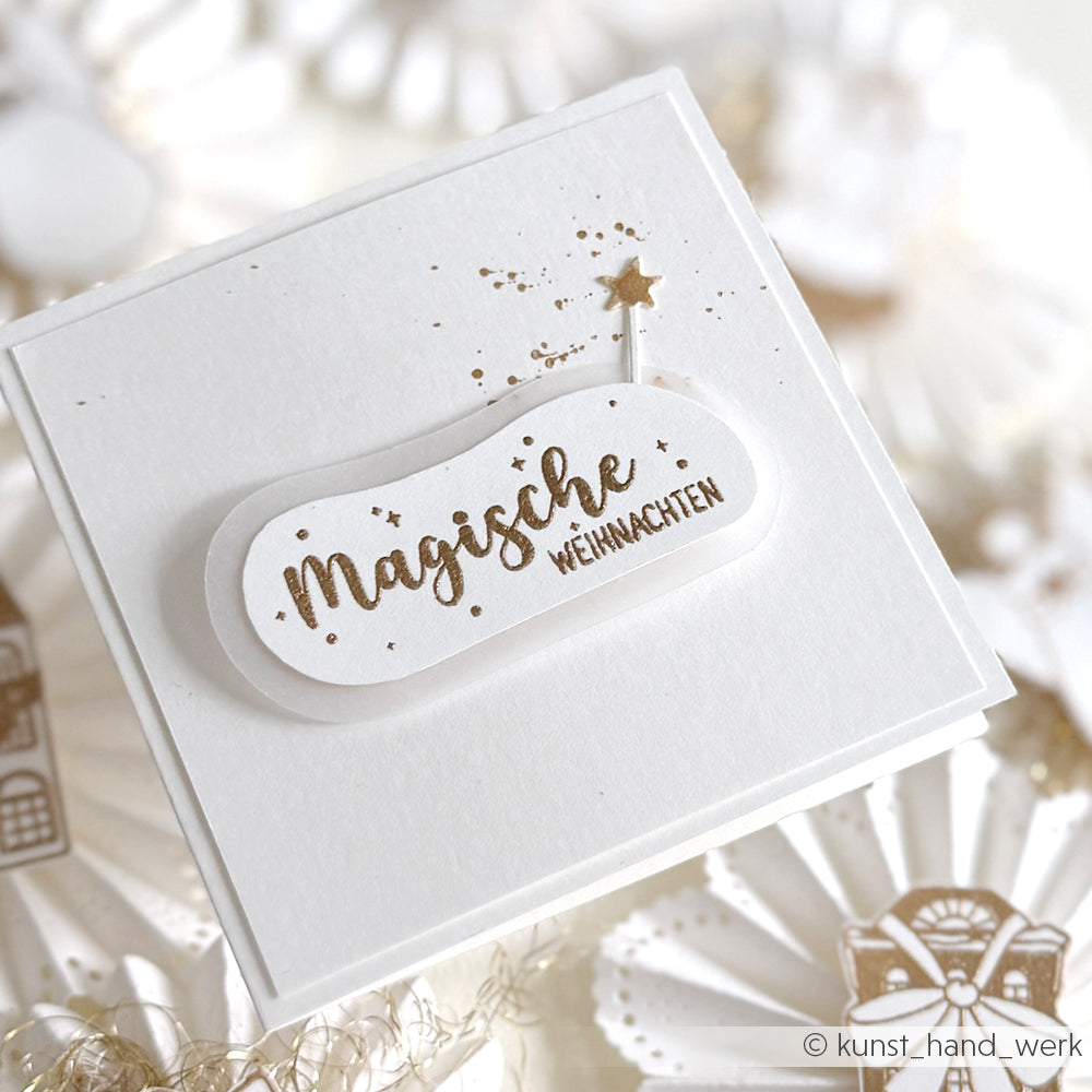 Weiße Karte von Alexandra Renke mit goldenem Text "Magische Weihnachten", gestempeltem Design und einem kleinen Stern auf weißem, festlichem Hintergrund.