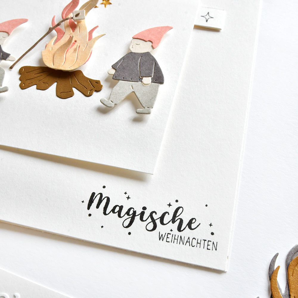 Handgemachte Karte von Alexandra Renke mit einem Gnom am Lagerfeuer, verziert mit Stempelgummi und dem Text "Magische Weihnachten".