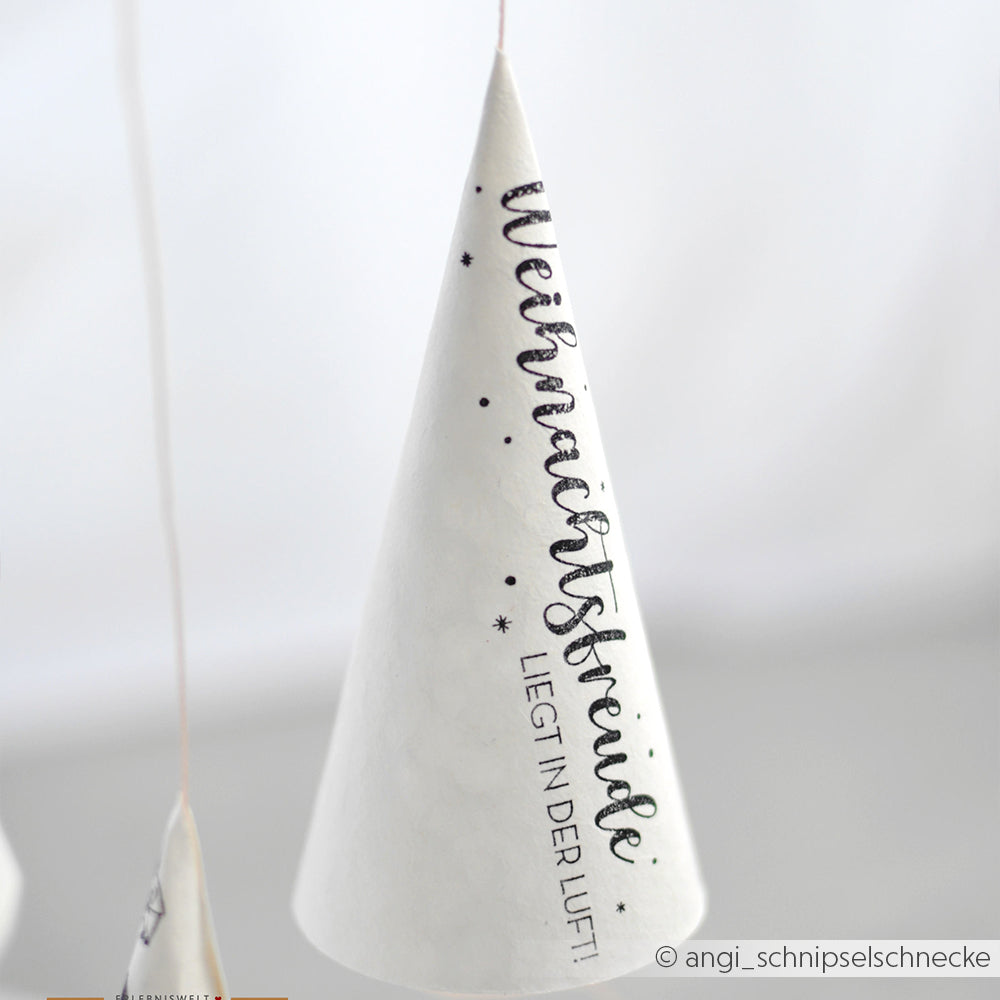 Der weiße Zapfenschmuck von Alexandra Renke mit der Aufschrift "Weihnachtsfreude liegt in der Luft!" hängt an einer Schnur und eignet sich ideal für festliche Dekorationen und die Kombination mit einem Holzstempel in der Weihnachtszeit.