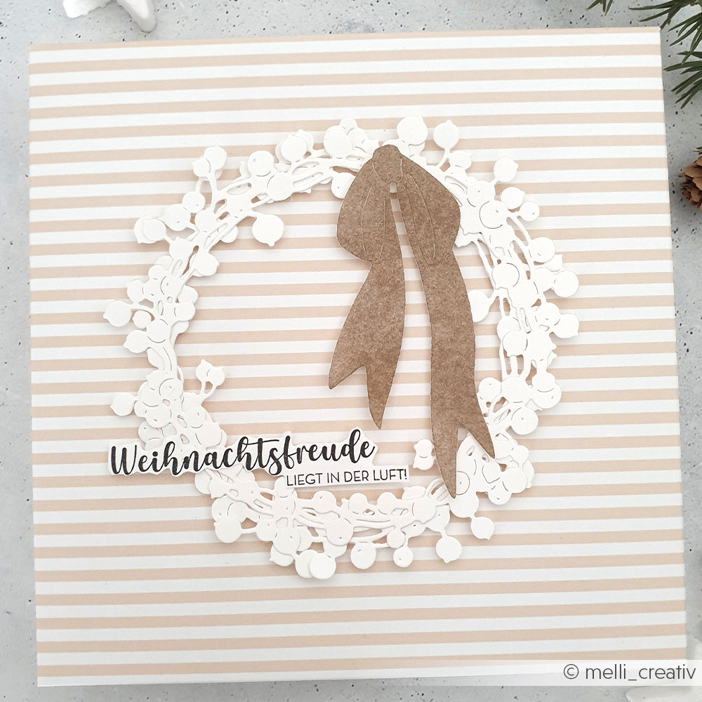 Ein weißer Papierkranz mit einer braunen Schleife auf einem beige gestreiften Hintergrund, mit deutschem Text in der Mitte, der Weihnachtsfreude bringt von Alexandra Renke.