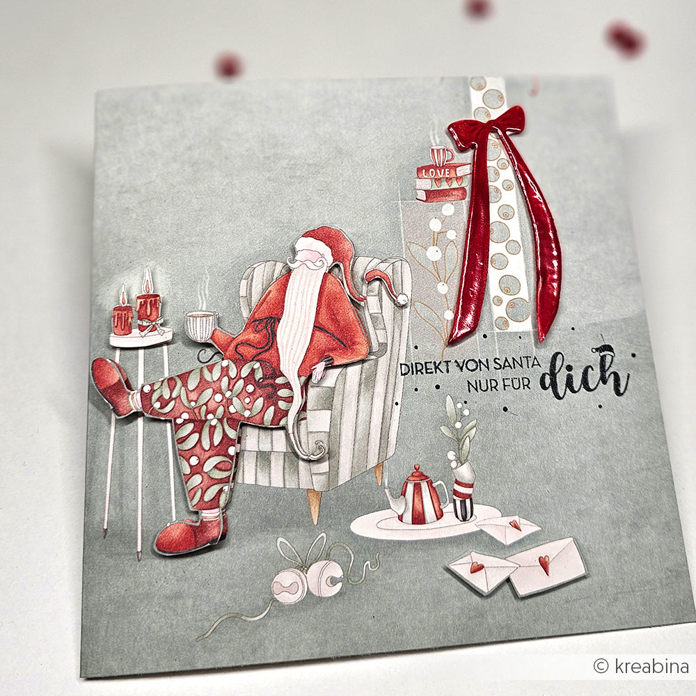 Der Weihnachtsmann im gemusterten Schlafanzug sitzt auf einem Stuhl mit Geschenken, Briefen, Tassen und einem Stempelkissen; der Text lautet "Direkt vom Weihnachtsmann nur für dich". Von Alexandra Renke.