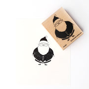 Alexandra Renke Holzstempel mit schwarzem Tintenaufdruck eines Cartoon-Weihnachtsmanns auf weißem Papier.