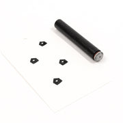 Ein kleiner zylindrischer Holzstempel und ein Stück Papier mit vier gestempelten Fünfecken, die mit einem „Mini Haus mit Herz“-Akzentstempel erstellt wurden.