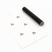 Ein schwarzer „Mini x-mas“-Stempel und ein weißes Geschenkanhängerchen, auf dem das Wort „x-mas“ fünfmal aufgestempelt ist.