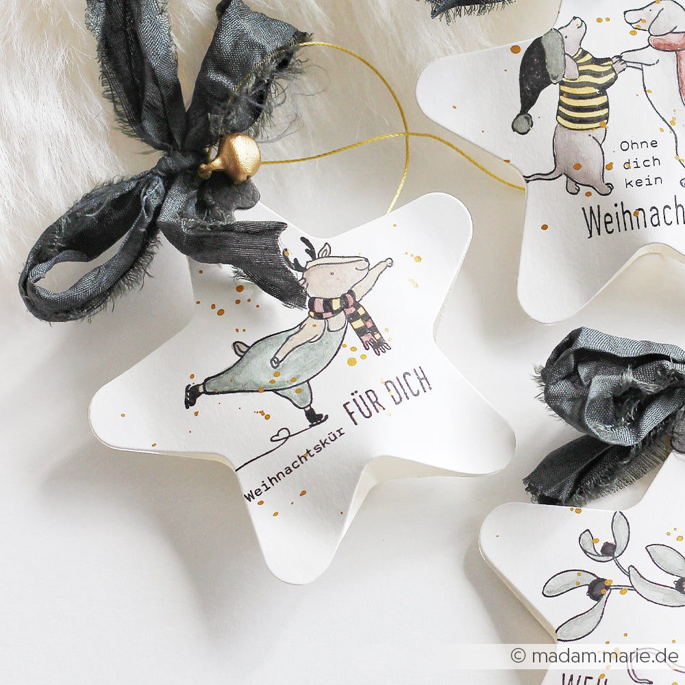 Sternförmiger Weihnachtsanhänger mit einem Eislaufenden Rentier, dem Schriftzug „Weihnachtskür FÜR DICH“ und festlichen Stempelmotiven.