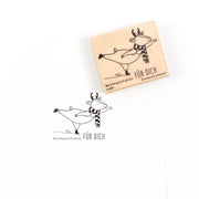 Ein hölzerner Weihnachtsstempel und sein Abdruck, der ein Schlittschuh laufendes Rentier zeigt, mit dem Text „Weihnachtskür FÜR DICH“.