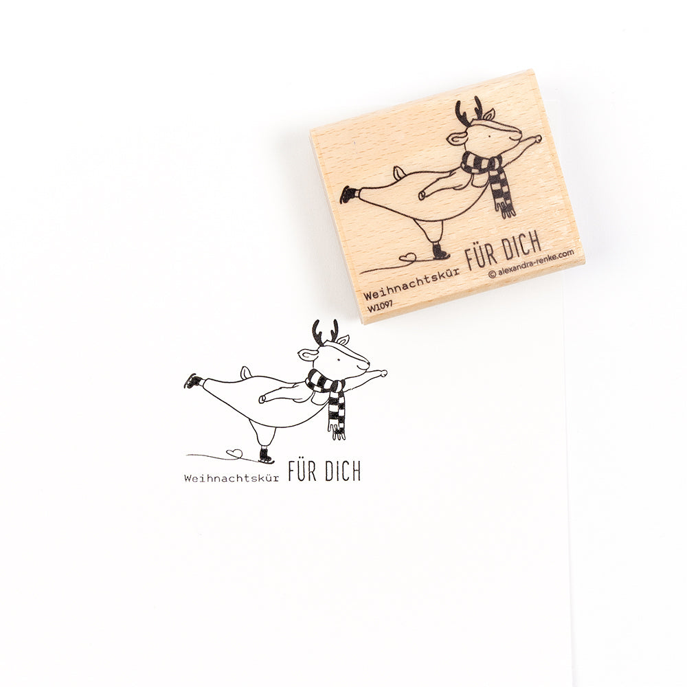 Ein hölzerner Weihnachtsstempel und sein Abdruck, der ein Schlittschuh laufendes Rentier zeigt, mit dem Text „Weihnachtskür FÜR DICH“.
