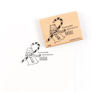 Ein Holzstempel mit der Abbildung eines Igels mit einer Zuckerstange und dem deutschen Text „Zuckersüße Weihnachts-GRÜBE“.
