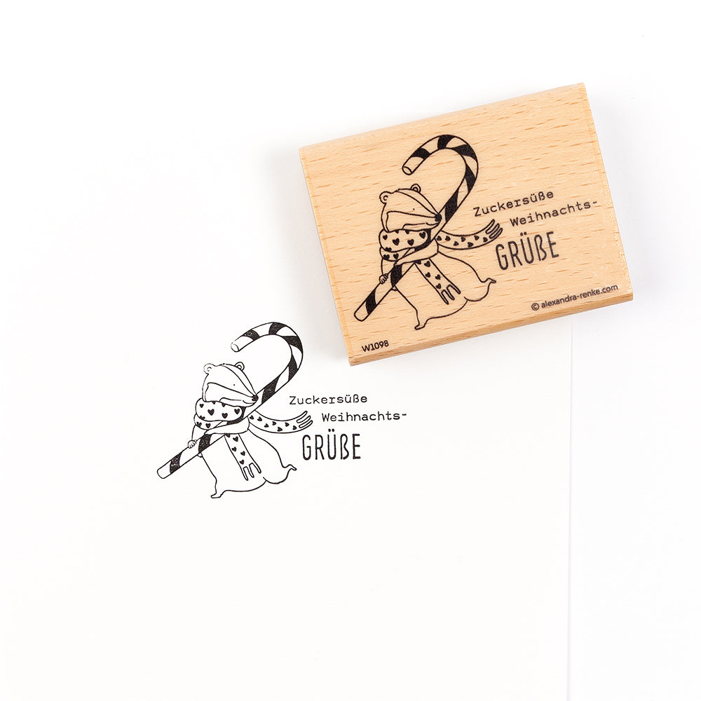 Ein Holzstempel mit der Abbildung eines Igels mit einer Zuckerstange und dem deutschen Text „Zuckersüße Weihnachts-GRÜBE“.