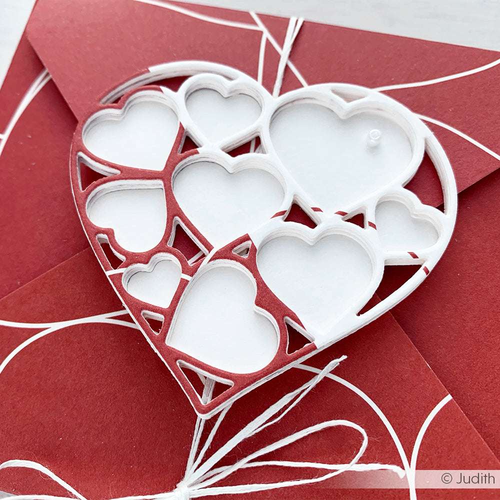 Eine herzförmige Karte von Alexandra Renke, die mit Motivstanze gefertigt wurde, zeigt weiße und rote ausgeschnittene Herzen auf einem roten Umschlag mit weißen Kordelakzenten - ideal, um Ihre Lieblingsdesignpapiere zu präsentieren.