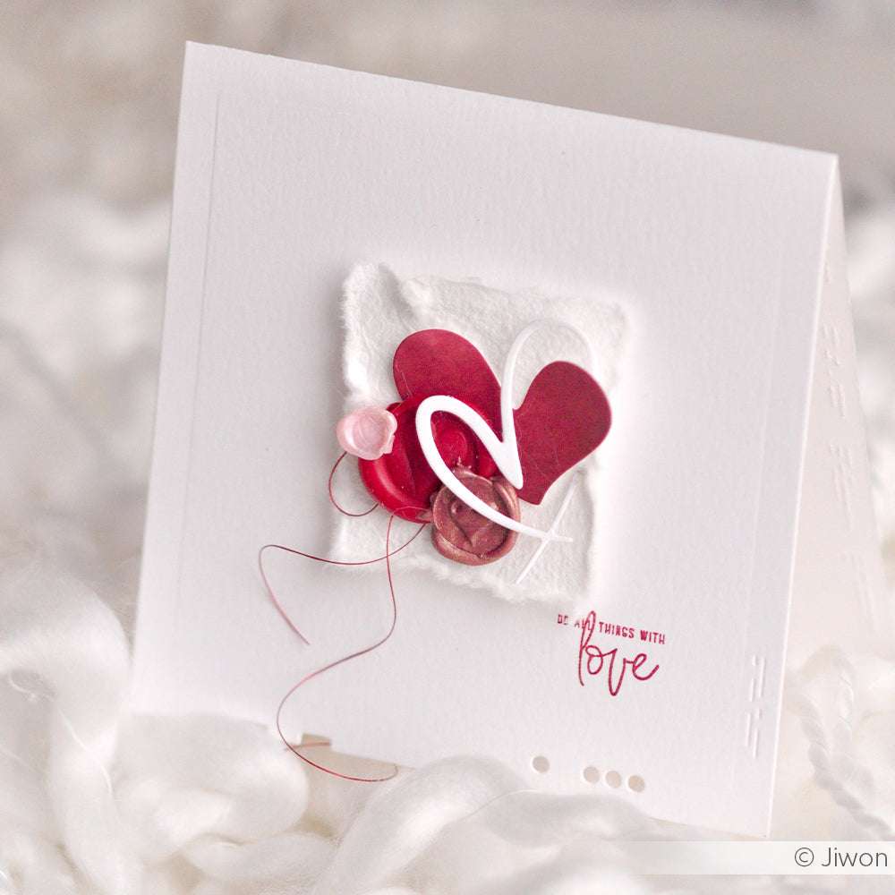 Handgefertigte Karte von Artist Herz 2 mit roten und rosafarbenen Herzen, die mit den Stanzformen von Alexandra Renke, Fadenakzenten und dem Wort "Liebe" in Rot auf weißem Papier übereinandergelegt wurden.