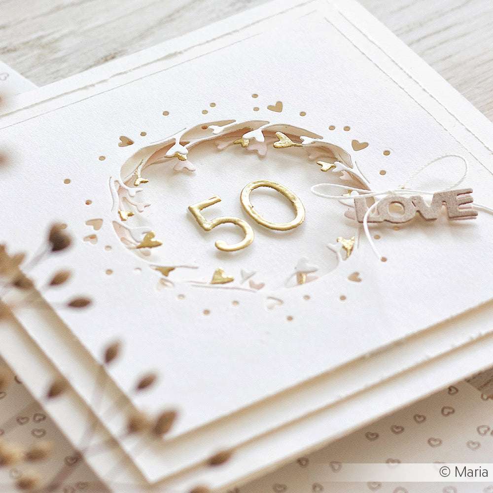 Elegante weiße Karte von Alexandra Renke mit Gold 50, einem zarten Herzkranz aus Motivstanzen und einer kleinen LOVE-Dekoration, die mit einer Schnur gebunden wird.