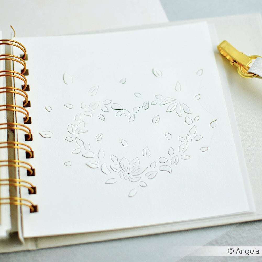 Ein weißes Alexandra-Renke-Blatt mit einem herzförmigen Blattausschnitt befindet sich in einem aufgeschlagenen Spiralheft, begleitet von einer goldenen Klammer.