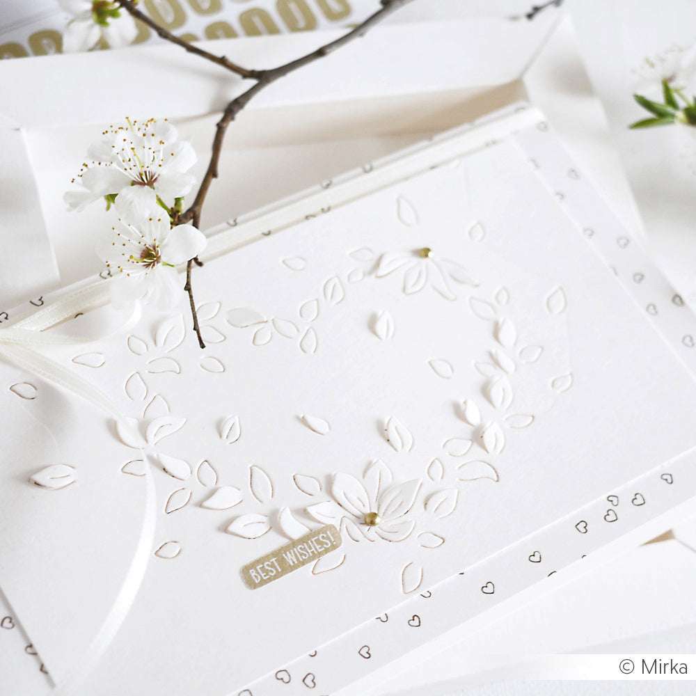 Weiße Prägekarte mit Blumenkranz, Schleife und dem Text "Beste Wünsche", hergestellt mit Alexandra Renke Design Papers und dem Motivstanze Negativ-Blütenherz-System. Abgerundet mit zarten weißen Blüten für einen eleganten Touch.