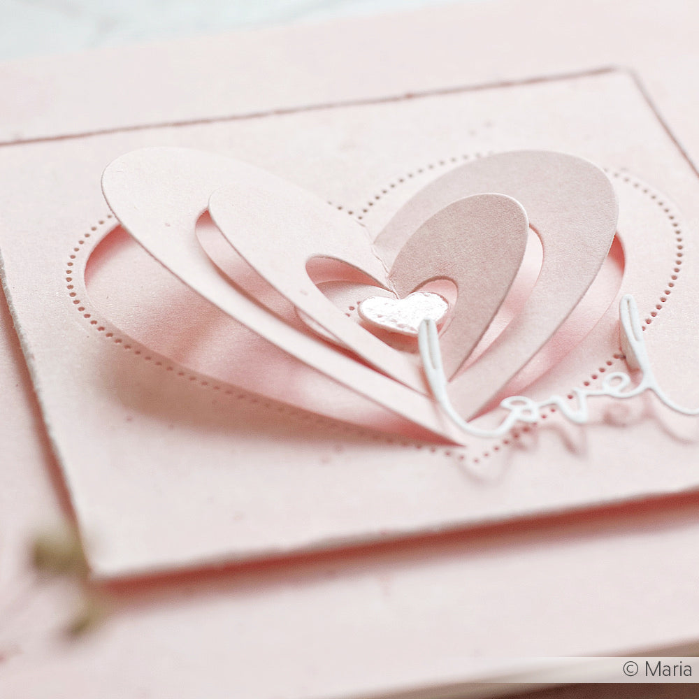 Ein geschichtetes rosa Papierherz, hergestellt mit Alexandra Renke DieCut Systeme, zeigt das Wort "Liebe" auf einer hellrosa Karte.