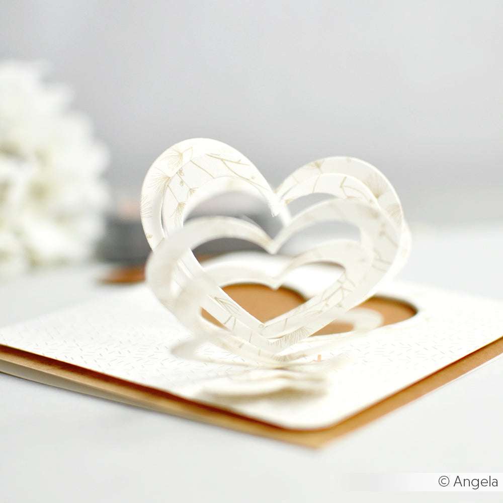 Pop-up-Grußkarte von Alexandra Renke mit ineinander verschlungenen weißen Herzen, gestaltet mit elegantem Designpapier auf strukturiertem weißem Hintergrund.