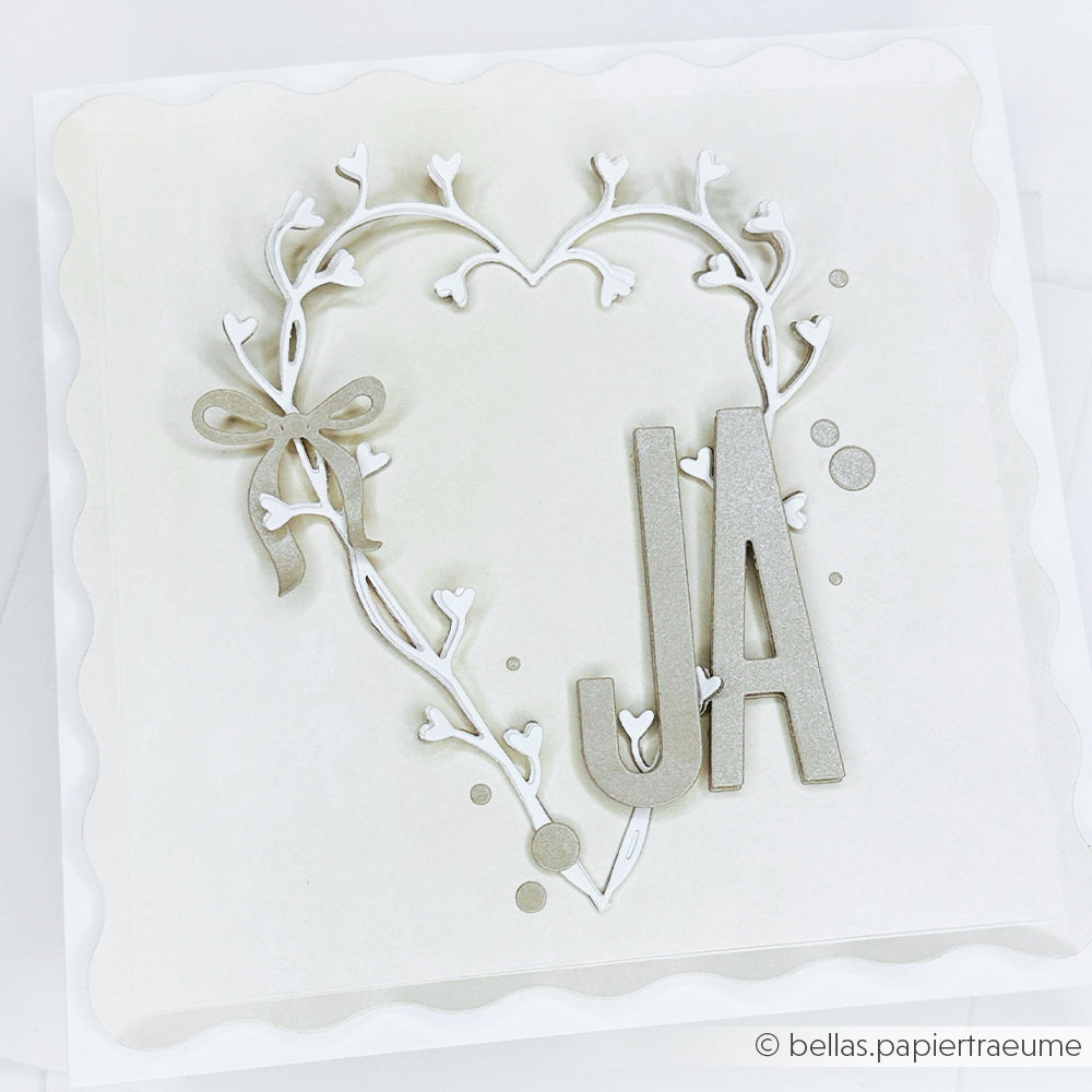 Weiße Karte von Alexandra Renke mit einer herzförmigen Ranke aus der Motivstanze Ranken-Herz, verziert mit einer zarten Schleife und großen JA-Buchstaben in sanften Neutraltönen.