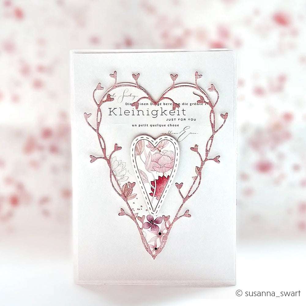 Grußkarte von Alexandra Renke mit herzförmigem Blumenmotiv aus Motivstanze Ranken-Herz und hochwertigen Designpapieren, hervorgehoben durch zartrosa Akzente auf einem weichen, verschwommenen Hintergrund.