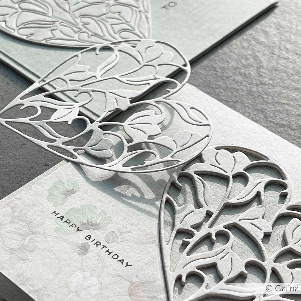 Nahaufnahme einer eleganten Geburtstagskarte von Alexandra Renke mit einem zarten Gefülltes Blumenherz-Motiv auf 200g Designpapier vor einem floralen Hintergrund.