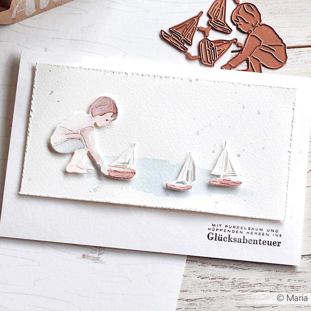 Die Karte von Alexandra Renke zeigt ein Kind, das mit drei Spielzeugsegelbooten auf dem Wasser spielt. Die Karte wird durch das passende Designpapier und ein gestanztes Element akzentuiert.