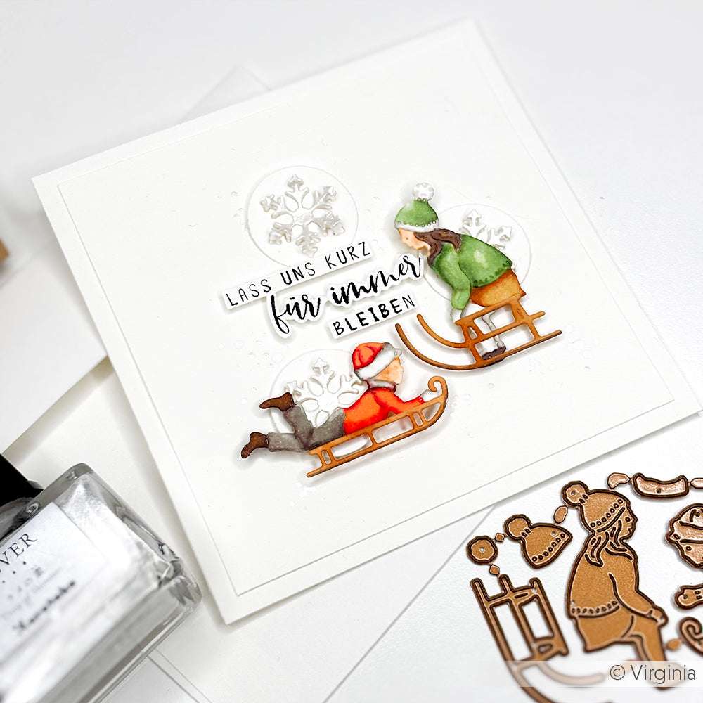 Handgemachte Karte von Alexandra Renke mit Schlittenkindern, deutschem Text und verschiedenen Designpapieren mit Bastelmaterial auf weißem Hintergrund.