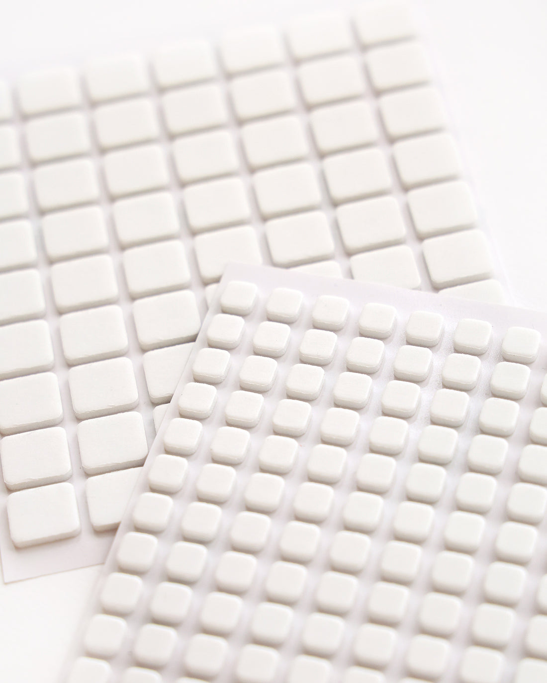 Blätter mit kleinen, weißen, quadratischen Schaumstoffblöcken, die in einem Raster auf einer weißen Fläche angeordnet sind.