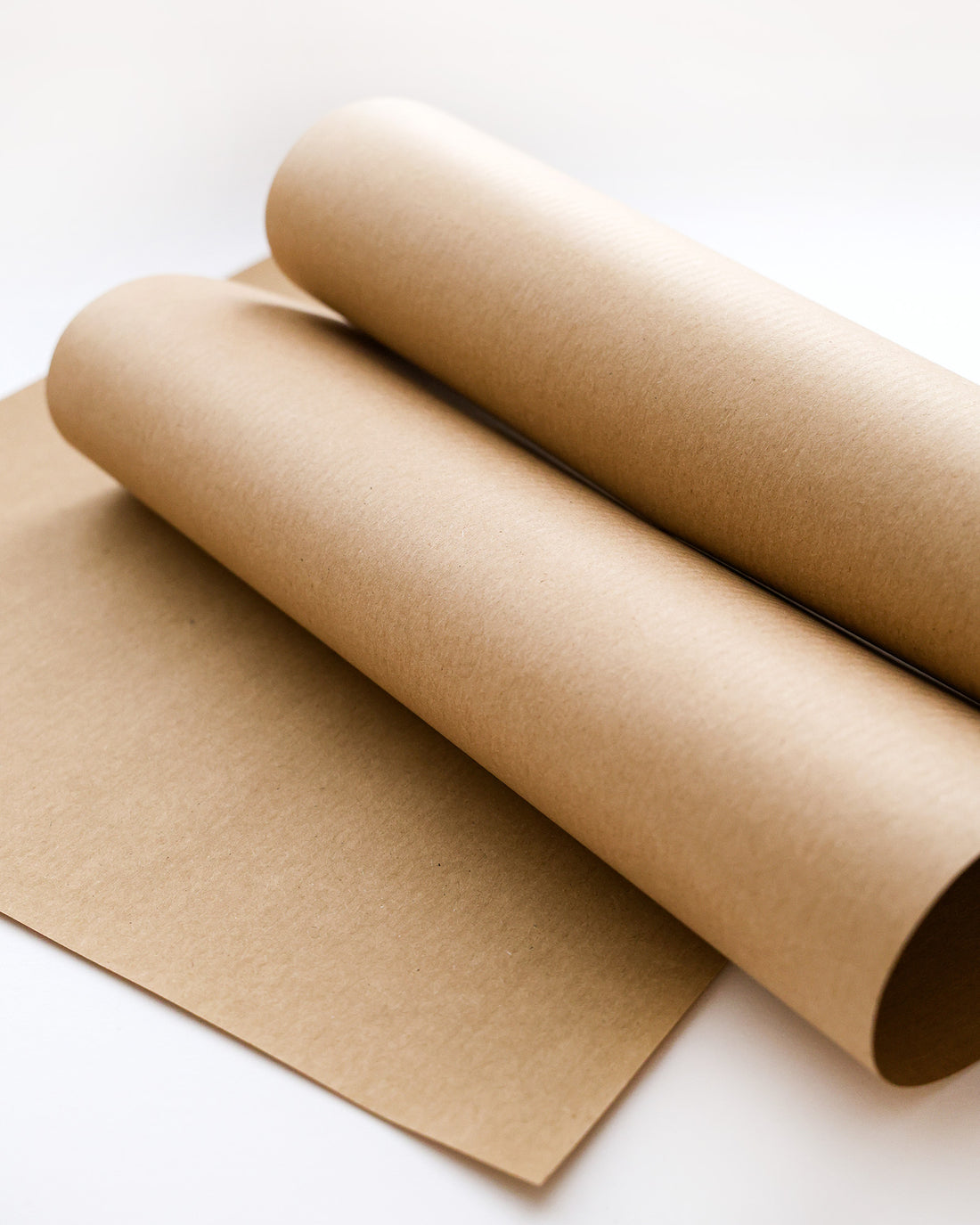 Zwei Rollen braunes Kraftpapier und ein flaches Blatt auf einer weißen Fläche.