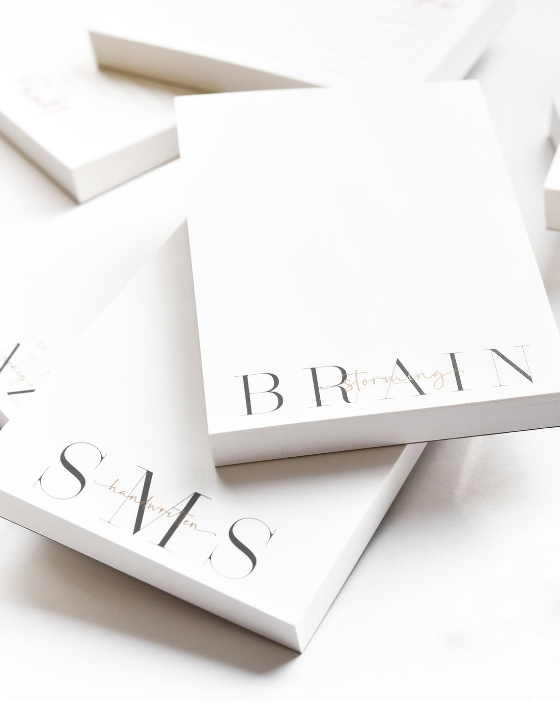 Stapel von minimalistischen Notizblöcken mit den Worten BRAIN STORMING und SMS am unteren Rand.