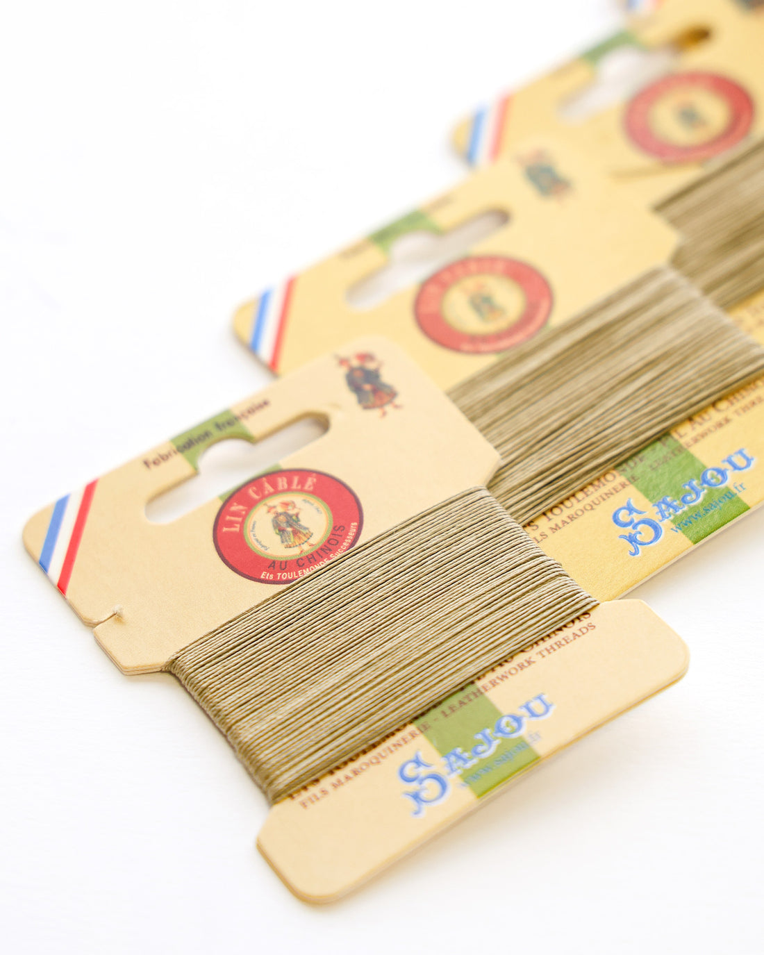 Vier Karten mit rosa Stickgarn sind diagonal auf einer weißen Fläche aufgereiht.