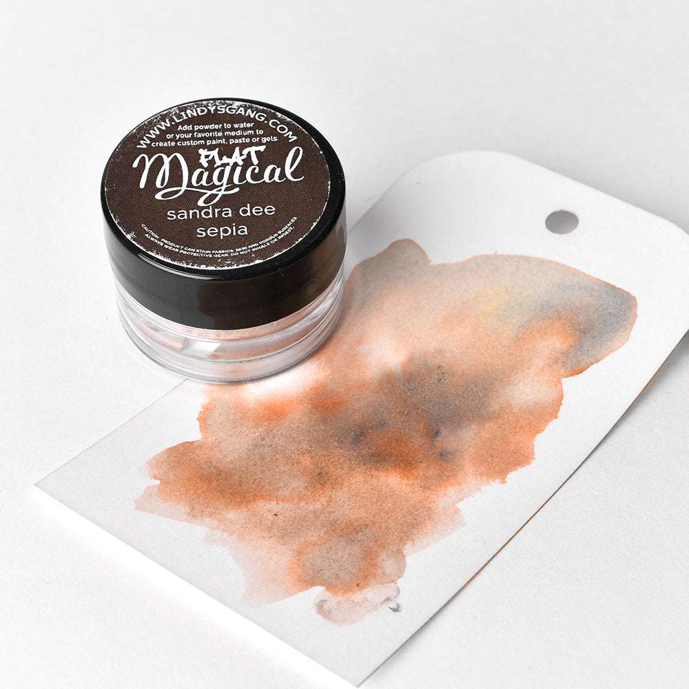 Eine kleine Dose Lindy's Stamp Gang Magical Powder, abgebildet mit einem sepiafarbenen Aquarellmuster auf einem weißen Anhänger - ideal für die Erstellung einzigartiger Farbmischungen.