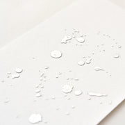 Weißes Strukturpapier mit glänzenden, unregelmäßig über die Oberfläche verteilten, erhabenen Punkten und Tupfen, veredelt durch Heißfolie für ein elegantes Finish.