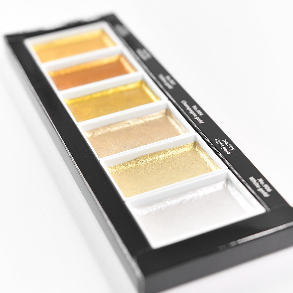 Eine Palette mit sechs Metallic-Aquarellfarben - Kuretake Gansai Tambi Starry Colors - in Gold-, Bronze- und Silberschattierungen auf Weiß. Erleben Sie die strahlende Schönheit der japanischen Aquarellfarben mit diesem schimmernden Set.