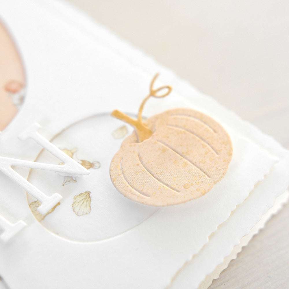 Nahaufnahme eines strukturierten, hellorangen Kürbisausschnitts auf einer weißen Karte, akzentuiert mit Kuretake Starry Colors Gold Aquarell und dekorativen Elementen.